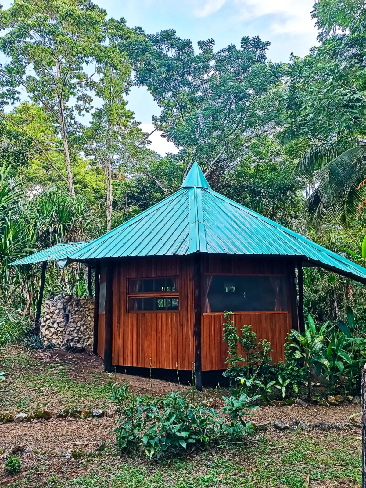 Toucan Cabana mit kegelförmigem Holzdach, umgeben von Heliconien